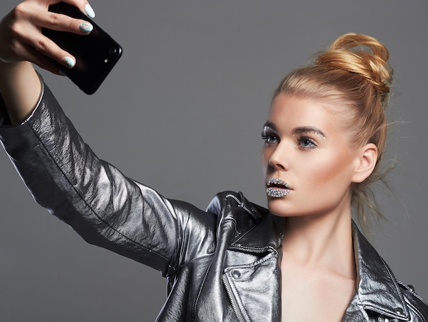 Hermosa mujer de moda con cristales en los labios con chaqueta plateada haciendo selfie