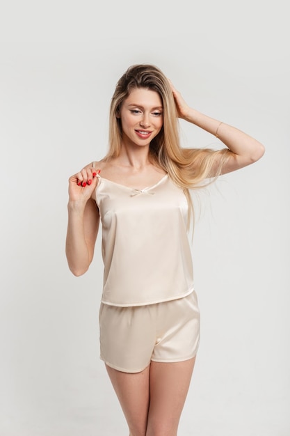 Hermosa mujer de moda con cuerpo esbelto en un elegante camisón beige con pantalones cortos y una camiseta elegante sobre un fondo blanco en el estudio