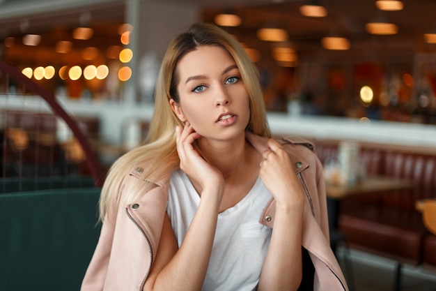 Hermosa mujer de moda en una elegante chaqueta rosa posando en un café