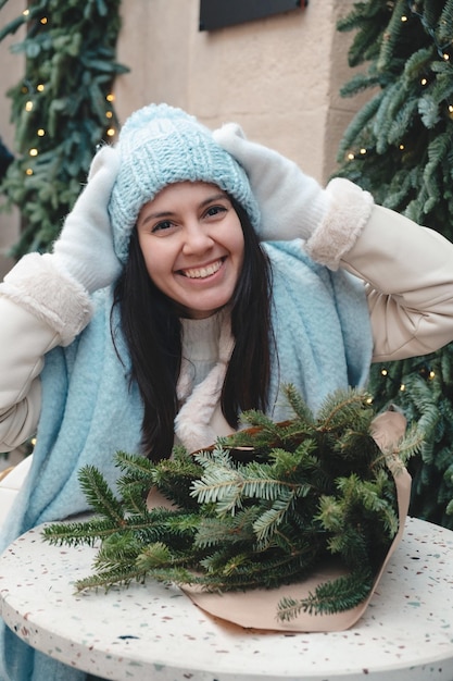 Hermosa mujer de moda sentada en la silla en un café al aire libre con un ramo de árboles de Navidad