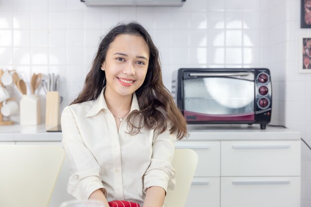 Hermosa mujer moderna sentada cerca de la mesa en la cocina de casa