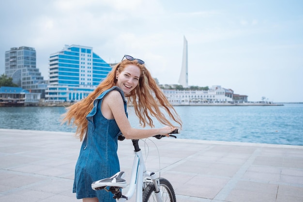 Hermosa mujer montando en bicicleta Estilo de vida y salud en la ciudad Alegre joven pelirroja disfruta caminando por la ciudad