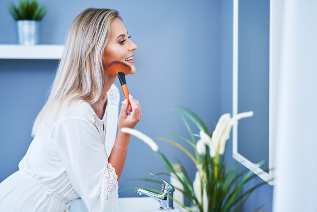 Hermosa mujer morena aplicar maquillaje en el baño.