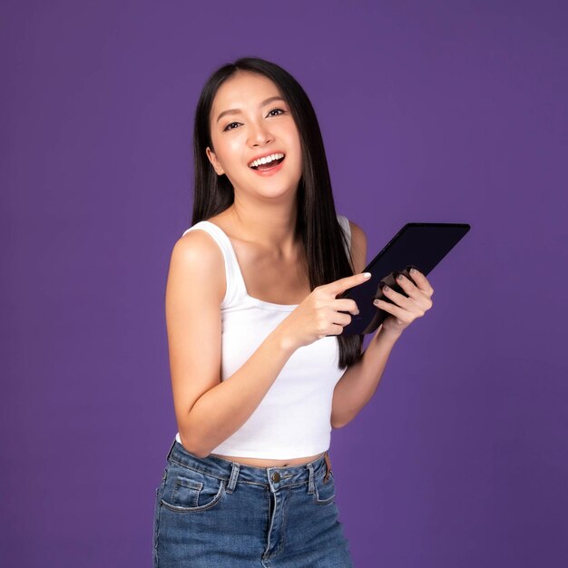 Hermosa mujer morena asiática linda chica en camiseta blanca tocando una tableta de teléfono inteligente aislada en un teléfono móvil de fondo púrpura utiliza una banca en línea para pagar compras en línea