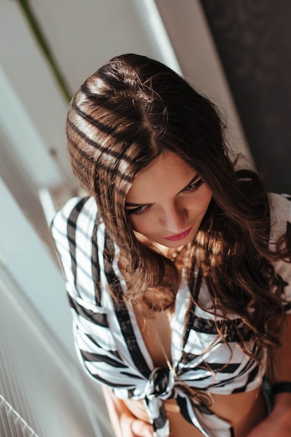 Hermosa mujer morena con cabello natural en pose sensual en la cama con camisa abierta y bragas blancas