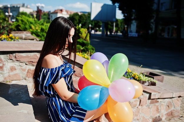 Foto hermosa mujer morena en la calle de la ciudad con globos en las manos.