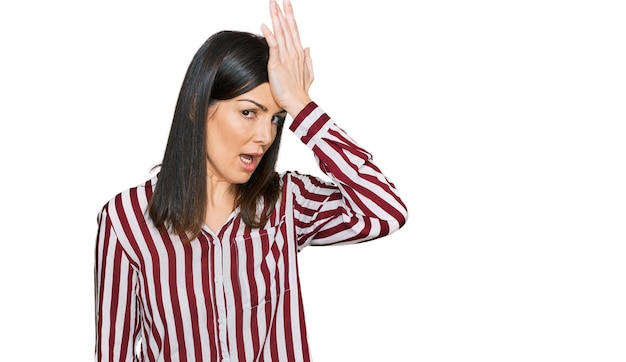 Hermosa mujer morena con camisa a rayas sorprendida con la mano en la cabeza por error, recuerda el error. olvidé, mal concepto de memoria.