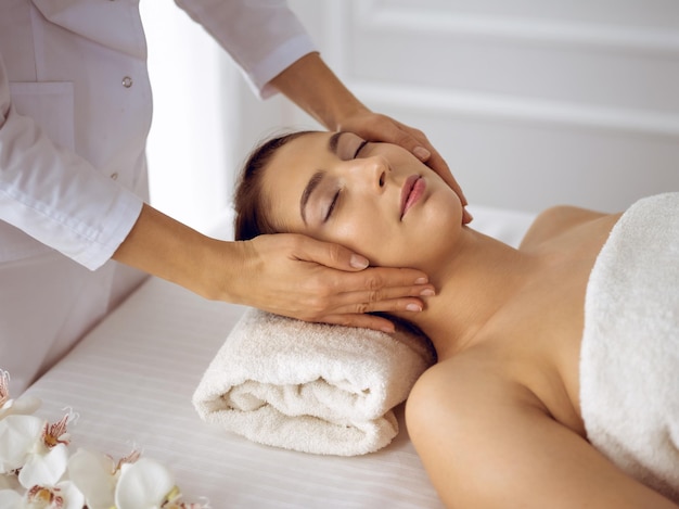 Hermosa mujer morena disfrutando de un masaje facial con los ojos cerrados. Tratamiento relajante en conceptos de centro de medicina y spa.