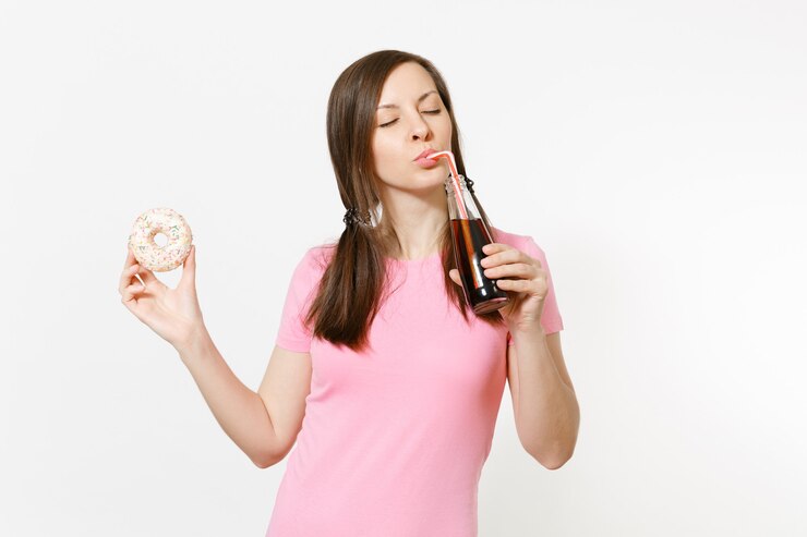 Foto hermosa mujer morena divertida sosteniendo en las manos coloridos donuts, cola en botella de vidrio aislada sobre fondo blanco. nutrición adecuada o dulces, postre, concepto de comida rápida. espacio publicitario para copiar espacio