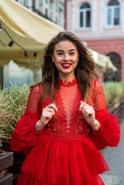 Hermosa mujer morena con estilo posando en vestido rojo en el fondo de la ciudad