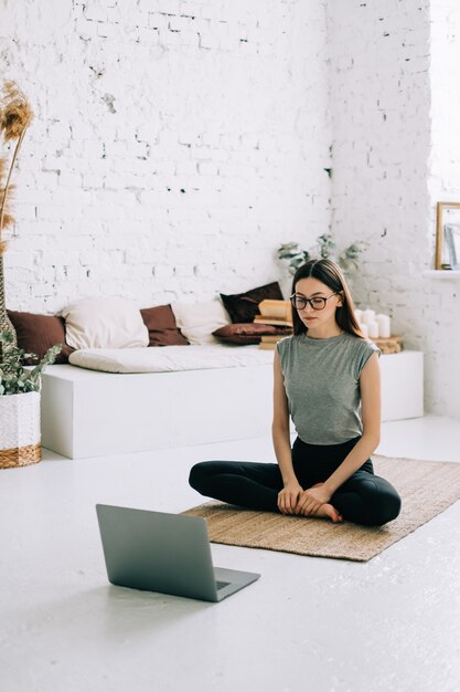 Hermosa mujer morena fitness meditar delante del portátil haciendo yoga en el interior en casa