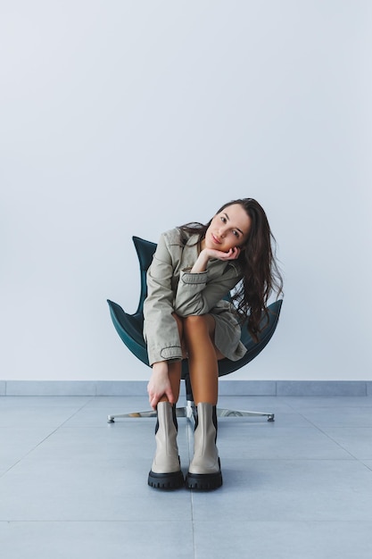 Hermosa mujer morena en una gabardina de otoño y botas de cuero posando en el estudio Moda femenina