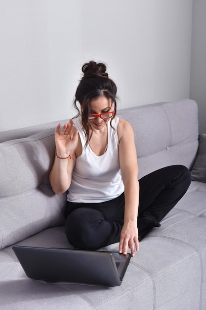 Hermosa mujer morena con gafas rojas en el sofá usando la computadora portátil