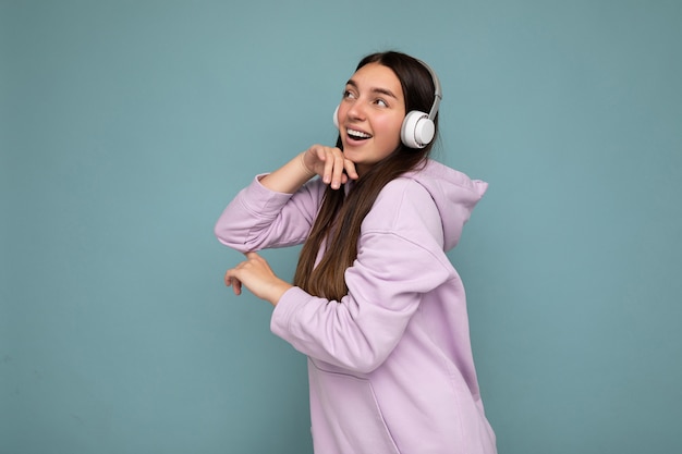 Hermosa mujer morena joven sonriente feliz vistiendo una sudadera con capucha de color púrpura claro aislado sobre fondo azul.