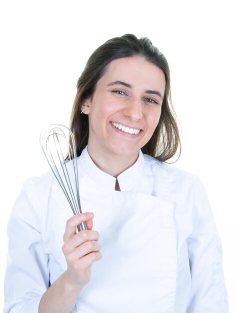 Hermosa mujer morena linda chef en uniforme de cocinero con batidor de mano sobre fondo blanco.