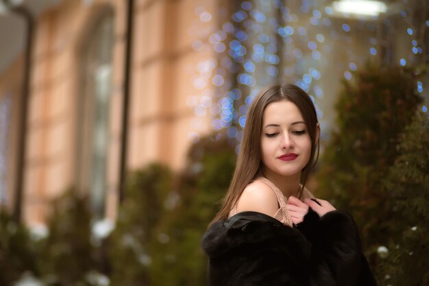 Hermosa mujer morena con los ojos cerrados, vestido con abrigo de piel, posando en el fondo de bokeh