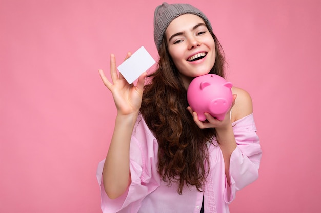 Hermosa mujer morena rizada joven alegre sonriente feliz vistiendo camisa rosa y sombrero gris aislado