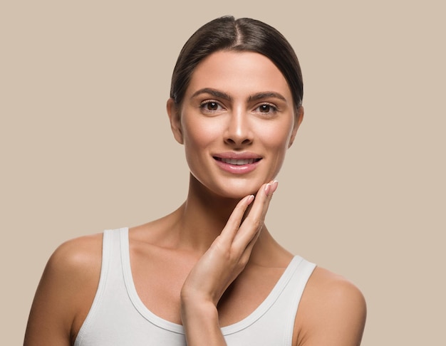 Hermosa mujer morena sana piel limpia maquillaje natural tocando la cara Fondo de color marrón