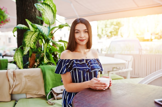 Hermosa mujer morena sentada en la mesa de café con taza de café.