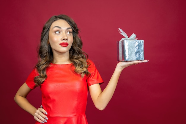 Hermosa mujer morena seria con un regalo en un fondo rojo