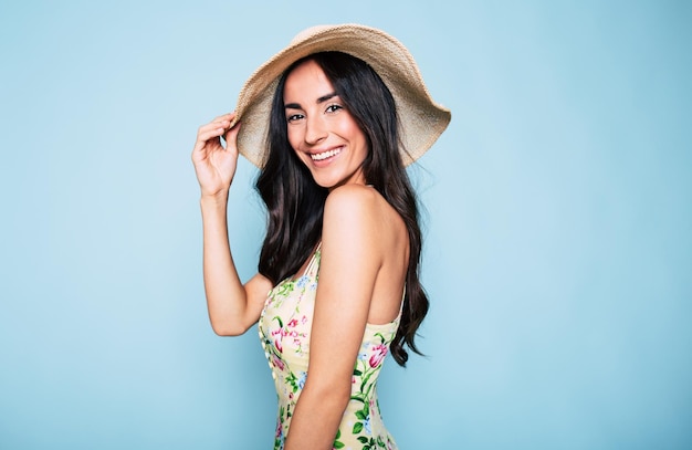 Hermosa mujer morena de verano con sombrero y vestido colorido chica elegante diviértete y posa sobre fondo azul