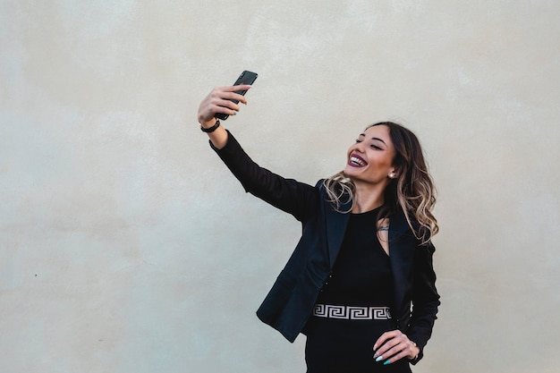 Hermosa mujer morena vestida elegante toma un selfie al aire libre. Mujer de negocios feliz.