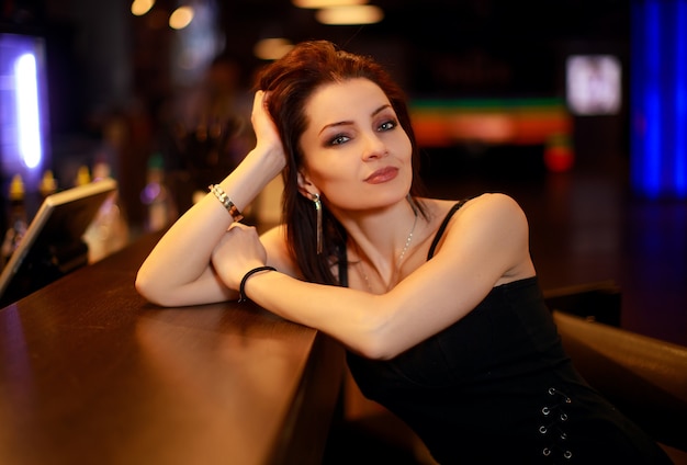 Hermosa mujer morena en vestido de noche posando junto a la barra sola