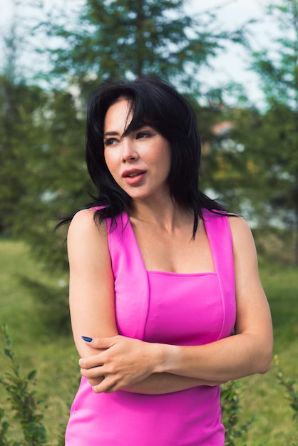 Hermosa mujer morena en vestido rosa posando en el parque