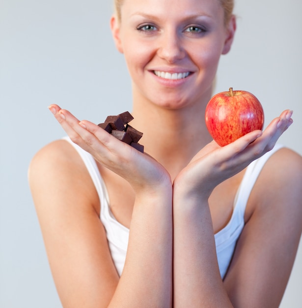 Hermosa mujer mostrando chocolate y manzana y mirando a la cámara se centran en chocolate y manzana