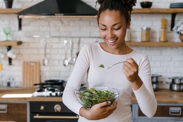 Hermosa mujer multirracial en forma comiendo ensalada saludable después del entrenamiento físico Chica feliz sosteniendo un plato grande con comida fresca en casa