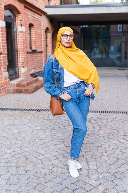 Hermosa mujer musulmana árabe con hijab amarillo, elegante retrato femenino sobre las calles de la ciudad.