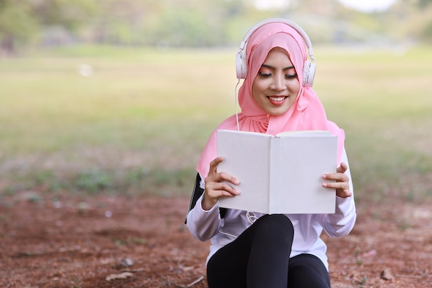 Hermosa mujer musulmana asiática fitness leyendo libro usando audífonos