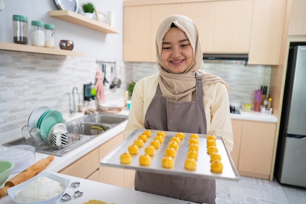 Hermosa mujer musulmana asiática con hijab haciendo torta nastar. bandeja llena de bocadillos caseros