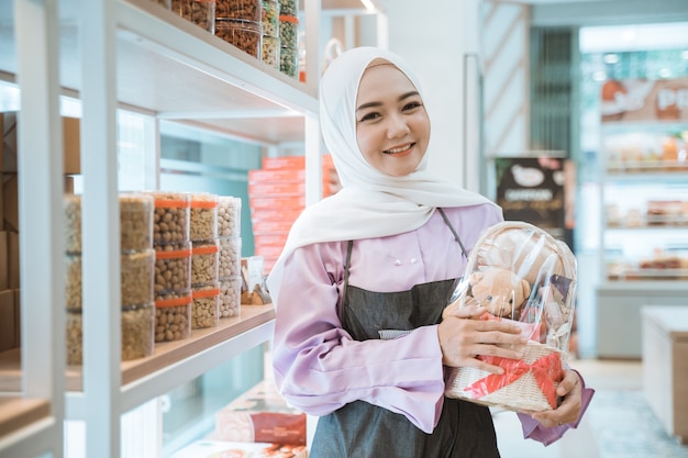 Hermosa mujer musulmana propietaria de la tienda sosteniendo un pastel para eid mubarak en su tienda