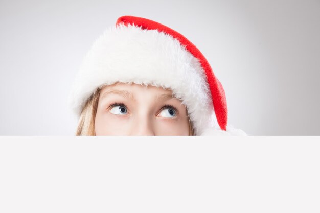 Hermosa mujer de Navidad con gorro de Papá Noel con tablero vacío y mirando a la derecha aislado sobre fondo blanco.