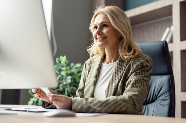 Hermosa mujer de negocios adulta madura con vestido elegante sentada en el escritorio de la computadora en la oficina