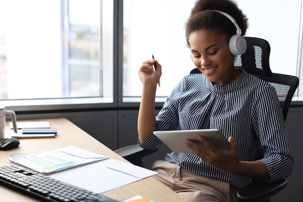 Hermosa mujer de negocios afroamericana está trabajando con tableta digital mientras está sentado en la oficina creativa.