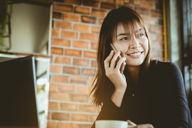 hermosa mujer de negocios de Asia hablando por teléfono móvil, bebiendo café sonríe con feliz.