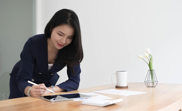 Hermosa mujer de negocios asiática analiza gráficos usando una calculadora portátil en la oficina