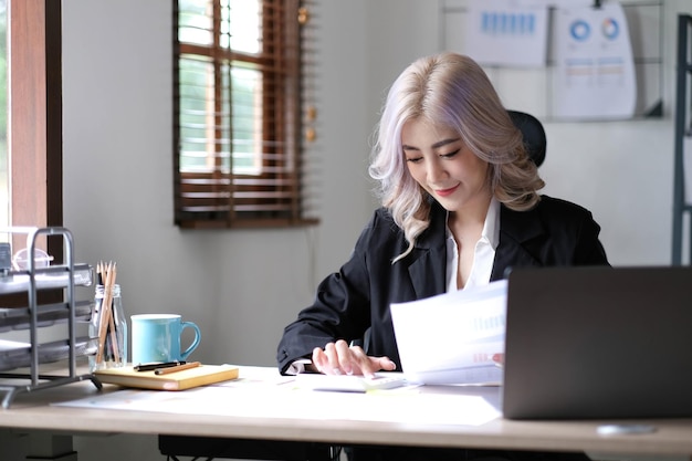 Hermosa mujer de negocios asiática analiza gráficos usando una calculadora portátil en la oficina