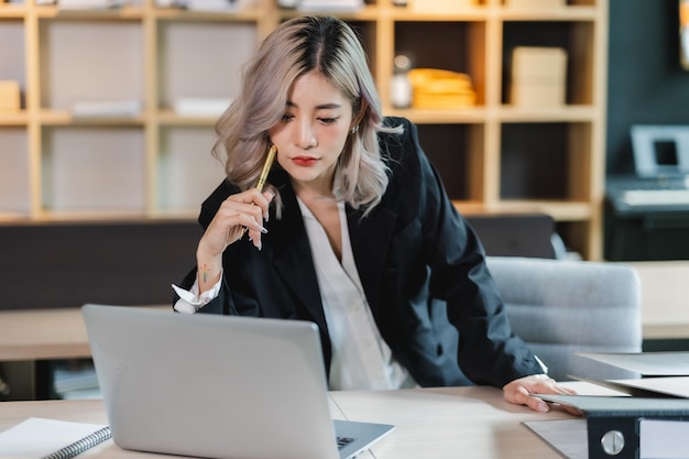 Hermosa mujer de negocios asiática que trabaja seriamente pensando en una idea para trabajar en una computadora y piensa en un proyecto para una idea sentada trabajando en interiores