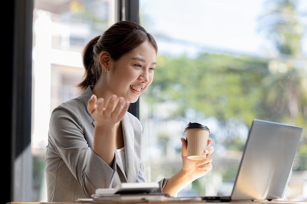 Hermosa mujer de negocios asiática sentada en su oficina privada, está hablando con su pareja a través de una videollamada en su computadora portátil, es una ejecutiva de una empresa nueva Concepto de gestión financiera