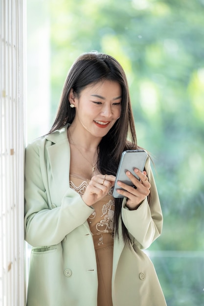 Hermosa mujer de negocios asiática sonríe y usa un teléfono inteligente trabajando Sonríe hermosa mujer asiática de negocios con traje trabajando en la oficina usando un teléfono inteligente