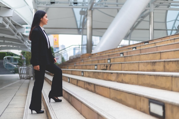 Hermosa mujer de negocios asiática con traje y pantalones camina al aire libre.