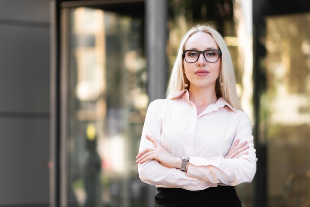 Hermosa mujer de negocios con una camisa, falda negra y gafas posando. Mira a la cámara al fondo de la entrada al centro de negocios.