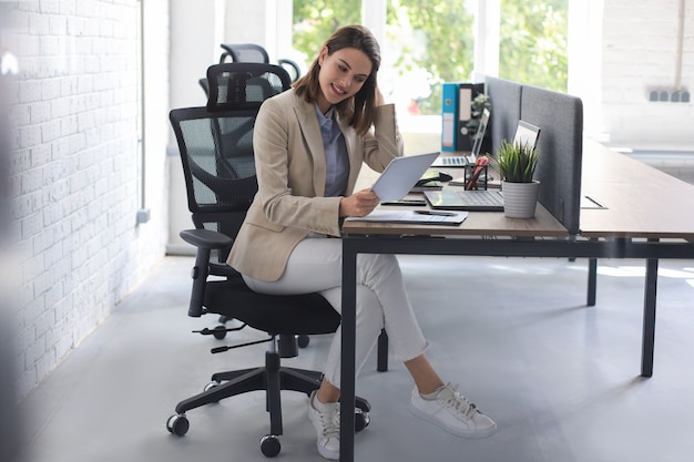 Hermosa mujer de negocios caucásica está trabajando con tableta digital mientras está sentado en la oficina creativa.