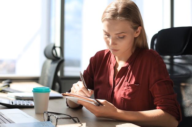 Foto hermosa mujer de negocios está escribiendo algo mientras está sentado en el escritorio de la oficina.