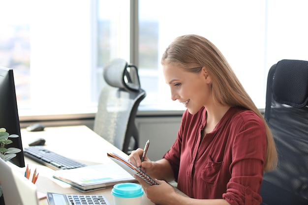 Hermosa mujer de negocios está escribiendo algo mientras está sentado en el escritorio de la oficina.