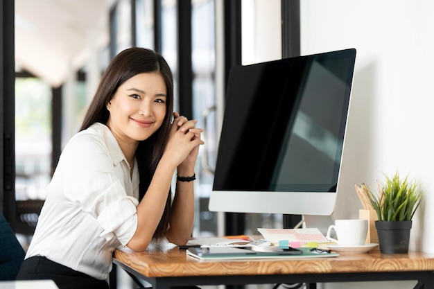 Una hermosa mujer de negocios está mirando a la cámara y sonriendo mientras trabaja en la oficina