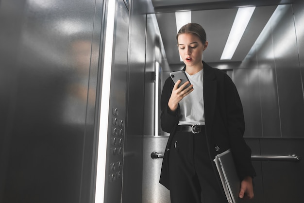 Hermosa mujer de negocios exitosa está usando su teléfono inteligente y sosteniendo una computadora portátil en su mano